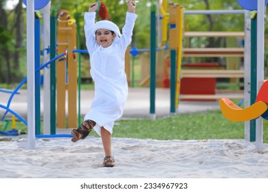 Young Arab Emirati boy at an outdoor playground. Arabic kid wearing Kandura dish dash. Middle Eastern child playing - Powered by Shutterstock