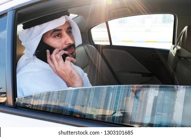 Young Arab Emirati Man Wearing Kandora Thobe While Holding His Cellphone Inside A Car Looking Outside The Window