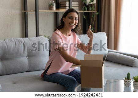 Young arab female loyal client of delivery service web shop open package show thumb up positive feedback. Portrait of indian lady blogger unpack box with ordered product look at camera recommend goods