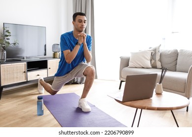 Young Arab Guy Doing Leg Exercises On Yoga Mat In Living Room Interior, Watching Online Workout On Laptop. Online Class, New Normal And Body Care At Home