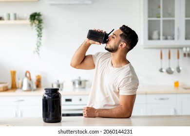 Young Arab guy drinking protein shake from bottle at kitchen, copy space. Millennial Eastern man using meal replacement for weight loss, having sports supplement for muscle gain. Body care concept - Shutterstock ID 2060144231