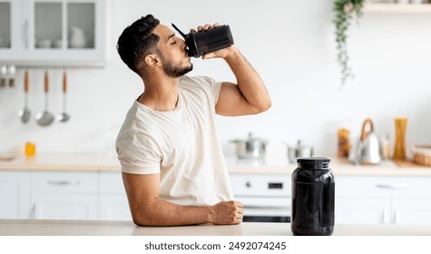 Young Arab guy drinking protein shake from bottle at kitchen, copy space. Millennial Eastern man using meal replacement for weight loss, having sports supplement for muscle gain. Body care concept - Powered by Shutterstock