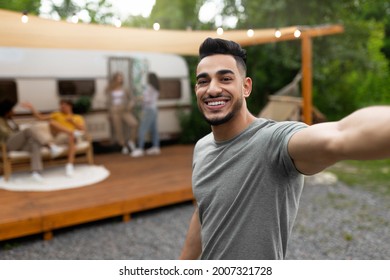 Young Arab guy taking selfie near motorhome, smiling at camera, resting on campsite with multiracial friends, creating happy memories, enjoying summer vacation outdoors, free space - Powered by Shutterstock