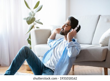Young Arab Guy In Wireless Headphones Enjoying Listening Music At Home, Millennial Eastern Man Sitting With Closed Eyes On Floor In Living Room, Having Rest With Favorite Melodies, Free Space