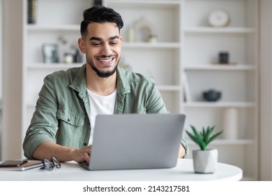 Young Arab Male Writer Working On Laptop At Home Office, Happy Millennial Middle Eastern Man Sitting At Desk And Typing On Keyboard, Guy Looking At Computer Screen And Smiling, Copy Space