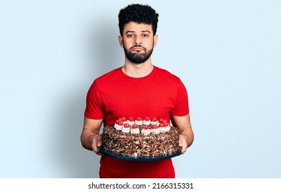 Young Arab Man With Beard Celebrating Birthday Holding Big Chocolate Cake Depressed And Worry For Distress, Crying Angry And Afraid. Sad Expression. 