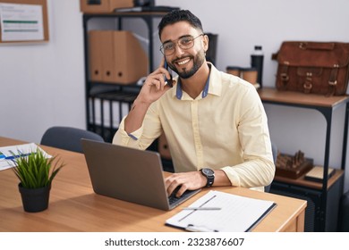 Young arab man business worker using laptop talking on smartphone at office - Powered by Shutterstock - Get 15% off with code: PIKWIZARD15