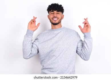Young Arab Man With Curly Hair Wearing Sport Sweatshirt
Over White Background Has Big Hope, Crosses Fingers, Believes In Good Fortune, Smiles Broadly. People And Wish Concept