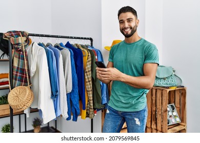 Young arab man customer using smartphone standing by clothes rack at clothing store