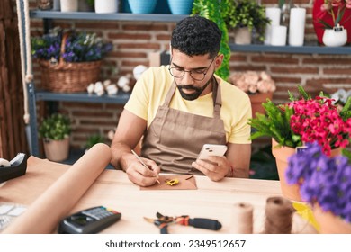 Young arab man florist writing on envelope letter using smartphone at florist - Powered by Shutterstock