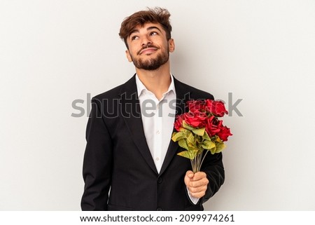 Young arab man holding bouquet of roses isolated on white background dreaming of achieving goals and purposes