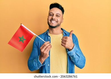 Young Arab Man Holding Morocco Flag Smiling Happy And Positive, Thumb Up Doing Excellent And Approval Sign 