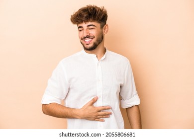 Young arab man isolated on beige background touches tummy, smiles gently, eating and satisfaction concept.