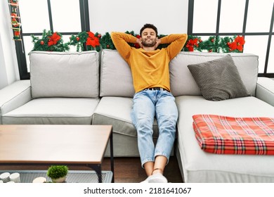 Young arab man relaxed with hands on head sitting on the sofa by christmas decoration at home.