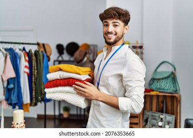 Young Arab Man Shopkeeper Holding Folded Clothes Working At Clothing Store