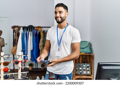 Young Arab Man Shopkeeper Paying With Credit Card And Data Phone At Clothing Store