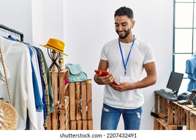 Young arab man shopkeeper using touchpad standing by clothes rack at clothing store