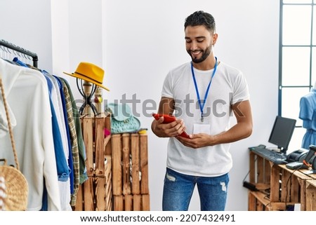 Young arab man shopkeeper using touchpad standing by clothes rack at clothing store