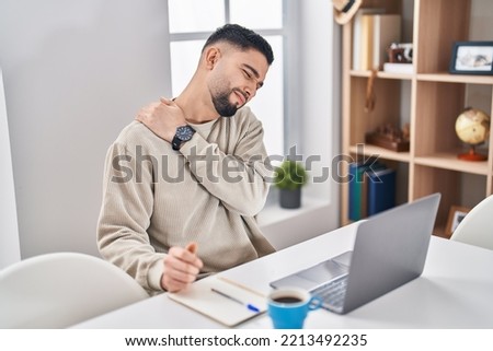 Young arab man suffering for back ache sitting on table working at home