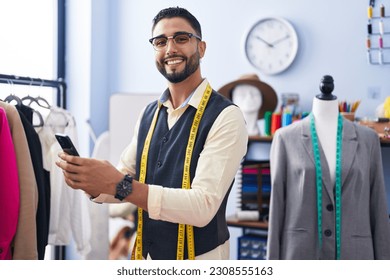 Young arab man tailor smiling confident using smartphone at clothing factory - Powered by Shutterstock