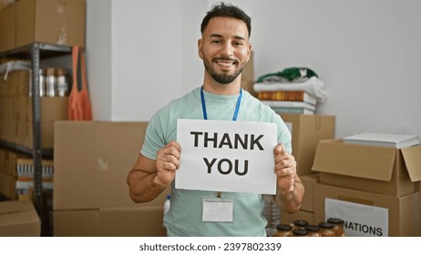 Young arab man volunteer holding thank you message smiling at charity center