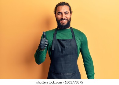 Young arab man wearing barber apron smiling happy and positive, thumb up doing excellent and approval sign  - Shutterstock ID 1801778875