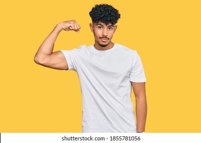 Young Arab Man Wearing Casual White T Shirt Strong Person Showing Arm Muscle, Confident And Proud Of Power 