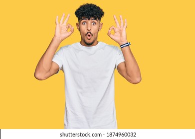 Young arab man wearing casual white t shirt looking surprised and shocked doing ok approval symbol with fingers. crazy expression 