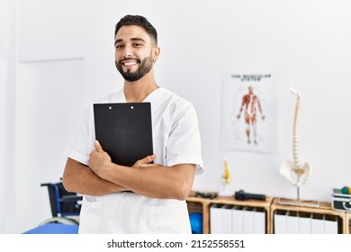 Young arab man wearing physiotherapist uniform holding clipboard at clinic - Shutterstock ID 2152558551