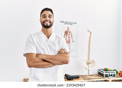 Young arab man wearing physiotherapist uniform standing with arms crossed gesture at clinic - Shutterstock ID 2193429457