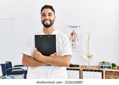 Young arab man wearing physiotherapist uniform holding clipboard at clinic - Powered by Shutterstock