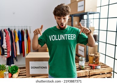 Young Arab Man Wearing Volunteer T Shirt At Donations Stand Pointing Down With Fingers Showing Advertisement, Surprised Face And Open Mouth 