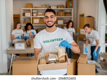 Young arab volunteer working at charity center, holding food donation box and smiling to camera. Man posing to camera in charity office - Powered by Shutterstock