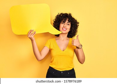 Young Arab Woman With Curly Hair Holding Speech Bubble Over Isolated Yellow Background Happy With Big Smile Doing Ok Sign, Thumb Up With Fingers, Excellent Sign