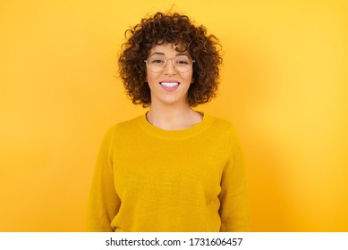 Young Arab woman with curly hair wearing yellow sweater over isolated yellow background with a happy and cool smile on face. Lucky person. - Powered by Shutterstock