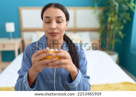 Young arab woman drinking cup of coffee sitting on bed at bedroom