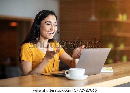 Young arab woman having business conference online, using laptop and headset, cafe interior, free space Stock photo © 