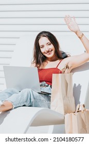 Young arab woman using his laptop doing online shopping outdoors during a bright day surrounded by shopping bags and smiling to camera about his new acquisitions. Happy shopping day renting concept Foto Stock