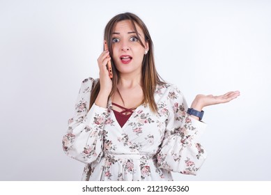 Young Arab Woman Wearing Floral Shirt Over White Backgtound Talking On The Phone Stressed With Hand On Face, Shocked With Shame And Surprise Face, Angry And Frustrated. Fear And Upset For Mistake.