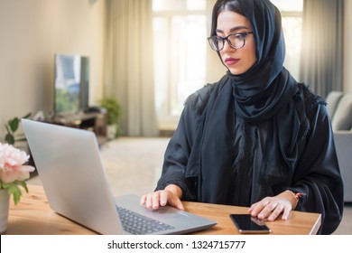 Young arab woman wearing hijab working on laptop at home.
