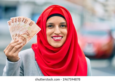 Young arab woman wearing hijab holding turkish lira banknotes at the city.