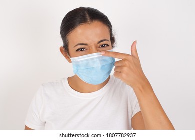 Young Arab Woman Wearing Medical Mask Standing Over Isolated White Background Pointing Unhappy To Pimple On Forehead, Ugly Infection Of Blackhead. Acne And Skin Problem