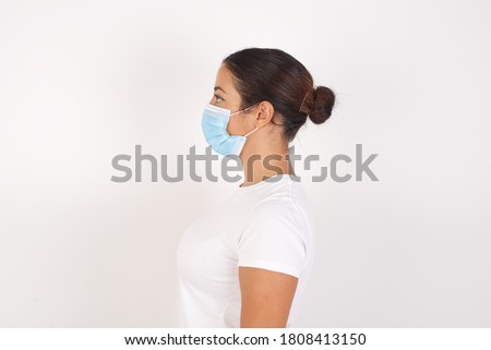 Young arab woman wearing medical mask standing over isolated white background looking to side, relax profile pose with natural face with confident smile.