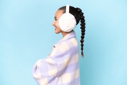 Young Arab Woman Wearing Winter Muffs Isolated On Blue Background In Lateral Position
