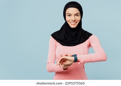 Young arabian asian muslim fitness trainer sporty woman wear pink abaya hijab spend time in home gym hold smart watch look camera isolated on plain blue background studio Workout sport fit abs concept - Powered by Shutterstock