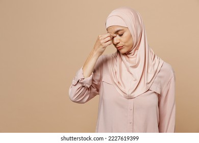 Young arabian asian muslim woman she wear abaya hijab pink clothes keep eyes closed rub put hand on nose isolated on plain pastel beige background. People uae middle eastern islam religious concept - Powered by Shutterstock