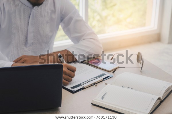 young Arabian business man signing contract on
insurance document with mobile phone and laptop computer on desk at
home office, life insurance, financial, successful business and
investment concept