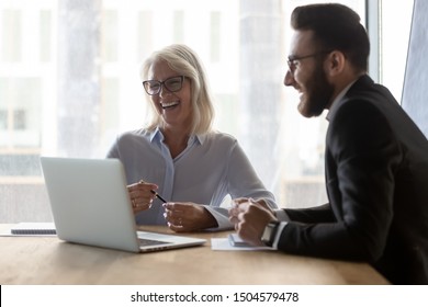 Young Arabian Colleague Helps To Older Woman With Pc App Office Workers Seated In Modern Boardroom Work Together, Make Video Call Distant Chat, Client And Boss Negotiation Positive Emotion Concept