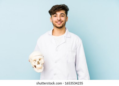 Young arabian doctor man holding a skull happy, smiling and cheerful.