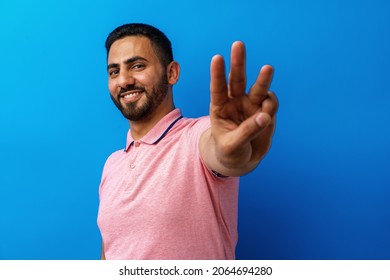 Young Arabian Man Smiling And Showing Three Fingers Against Blue Background